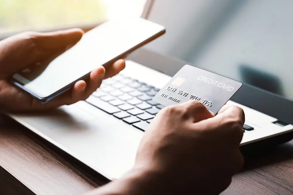 hands holding phone and credit card with laptop